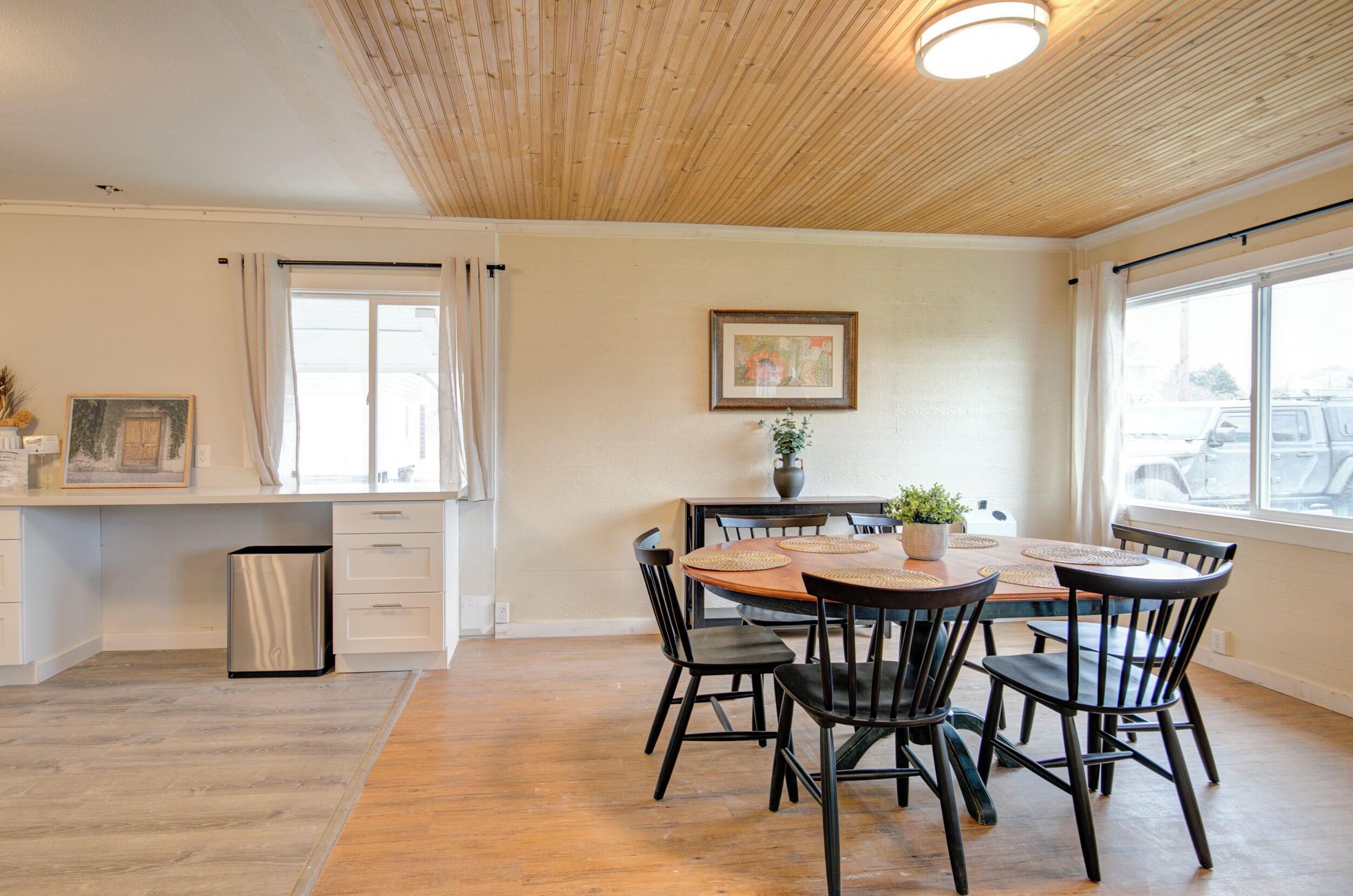 A dining area with a wooden table, black chairs, and a vase with a plant.