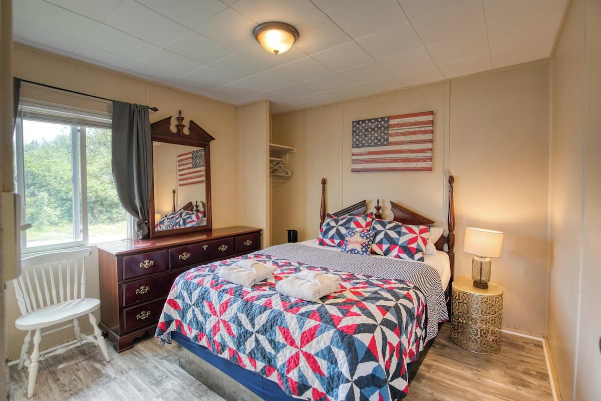 A bedroom with a large bed, a dresser, a chair, and an American flag on the wall.
