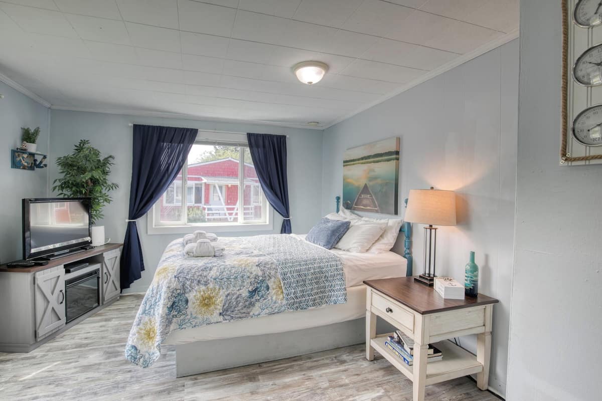 A bedroom with a bed, a TV, a lamp, and a window with curtains.