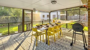 En overdækket terrasse med et spisebord, gule stole og en grill.