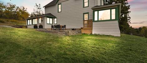 Une maison à deux étages, avec des fondations en pierre, un patio couvert et une pelouse bien entretenue.