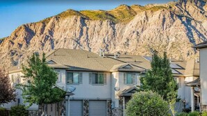 A two-story house with a garage, surrounded by greenery and a mountainous backdrop. - 30% OFF PROMO! East Ogden Dream, Newly Built, BBQ, Patio, Views, Dedicated Spa! (Ogden)