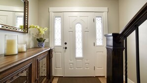 A hallway with a white door, a wooden console table with candles, a vase with flowers, and a black staircase. - 30% OFF PROMO! East Ogden Dream, Newly Built, BBQ, Patio, Views, Dedicated Spa! (Ogden)