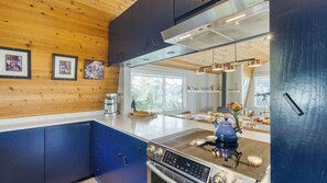 A modern kitchen with a stainless steel stove, wooden cabinets, and a large window. - Stunning Ocean Views, Steps to Beach Tranquil Retreat Cove Keep by Avantstay (Arch Cape)