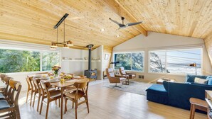 Een ruime loft met hoge plafonds, houten balken, een eethoek met tafel en stoelen, een gezellige zithoek met een bank, en grote ramen met uitzicht op de omgeving.