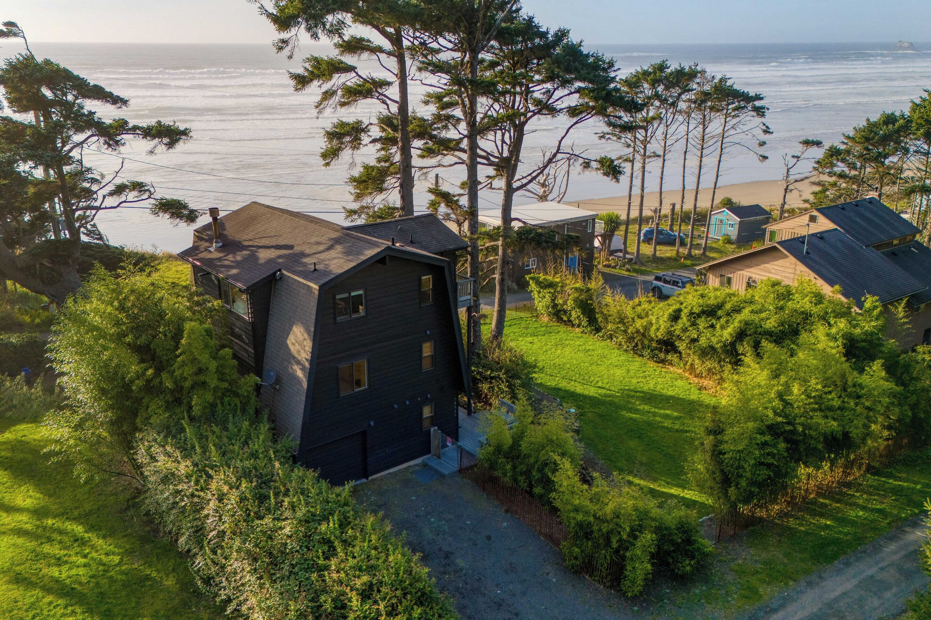 A coastal house with a dark exterior, surrounded by lush greenery and a view of the ocean.