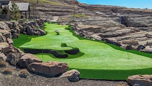A golf course with a green fairway, bunkers, and a rocky backdrop.