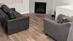 A modern living room with a fireplace, a flat-screen TV mounted above it, and two sofas. - City Retreat, 2 bdrm near Airport (Anchorage)