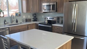 A modern kitchen with wooden cabinets, stainless steel appliances, a large island, and bar stools. - City Retreat, 2 bdrm near Airport (Anchorage)