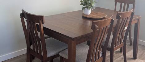 A dining room with a wooden table and chairs, a potted plant, and a framed picture on the wall.