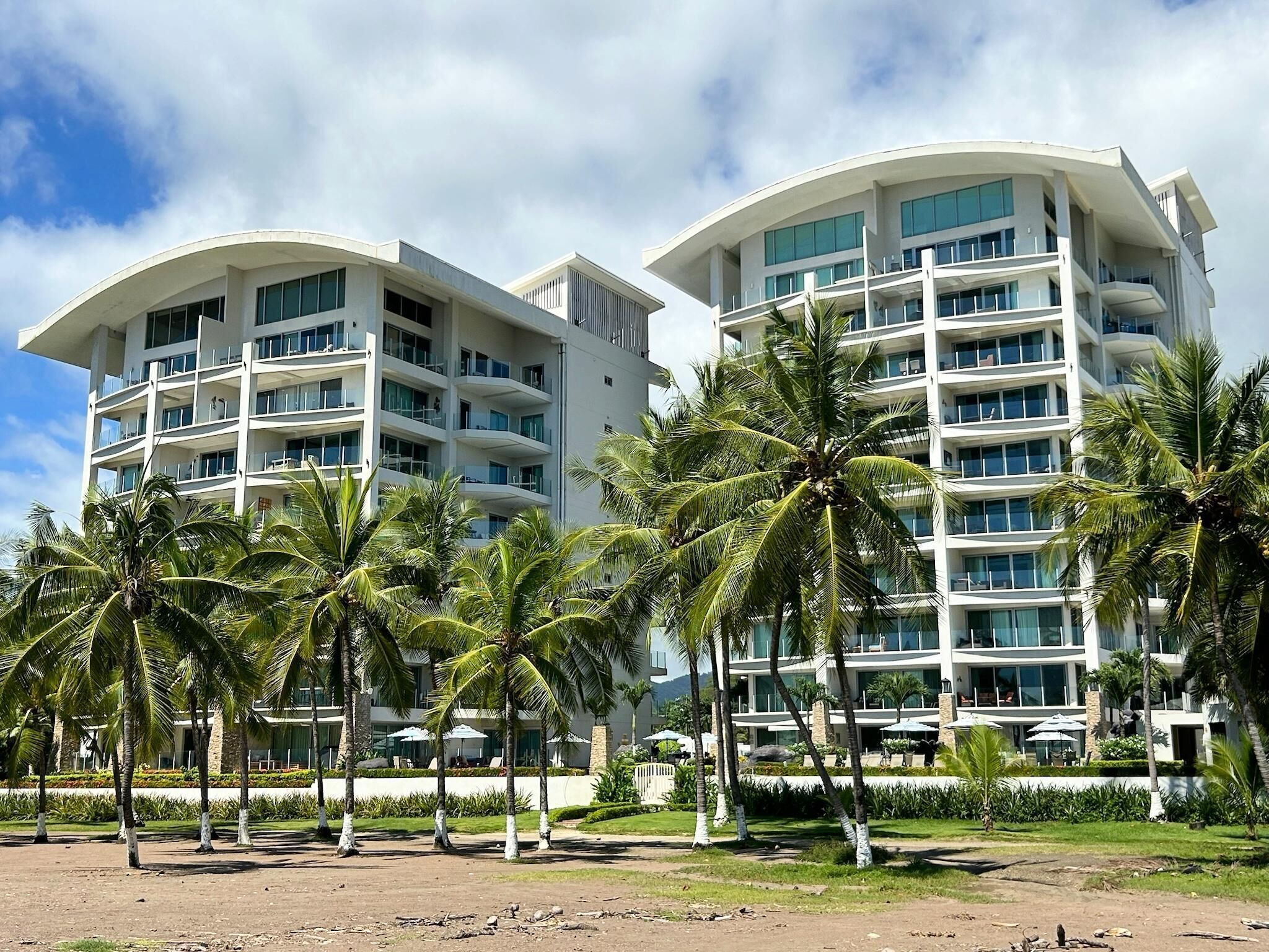 A modern hotel with multiple floors, balconies, and palm trees in the foreground.