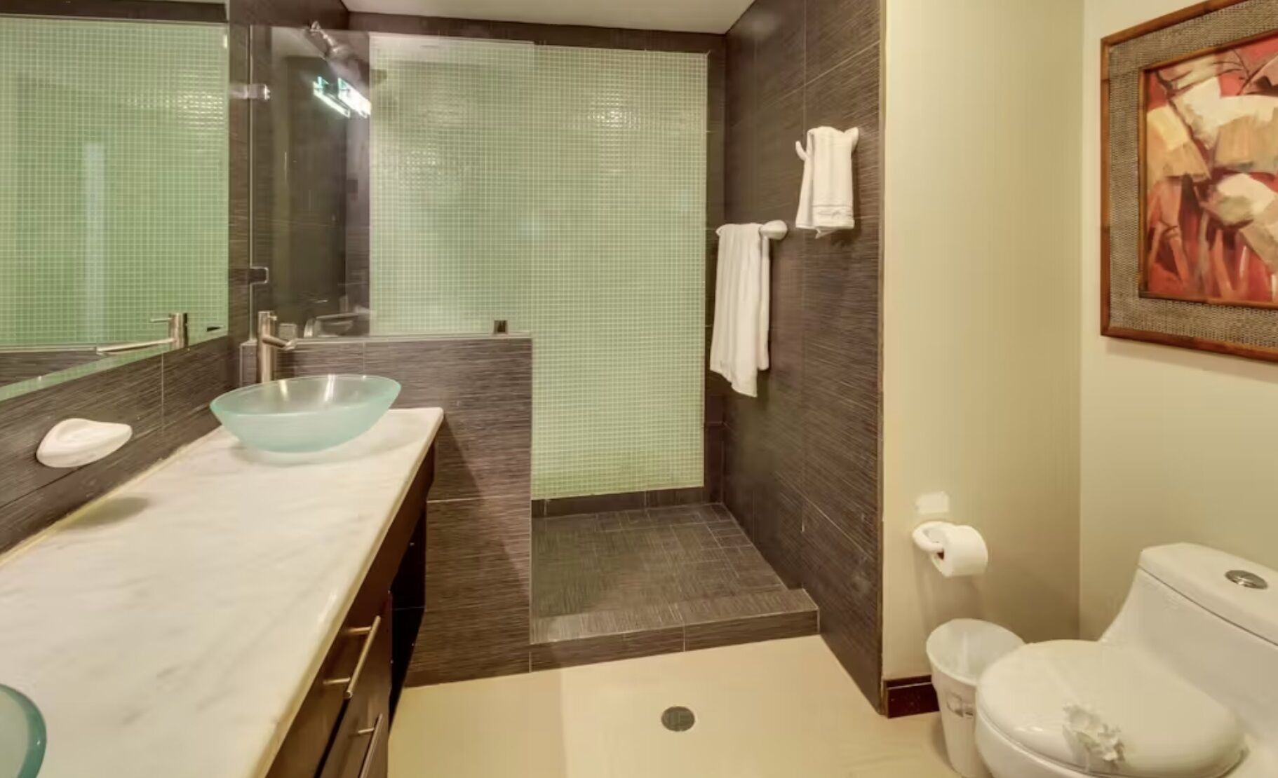 A bathroom with a glass bowl sink, a shower, and a toilet.