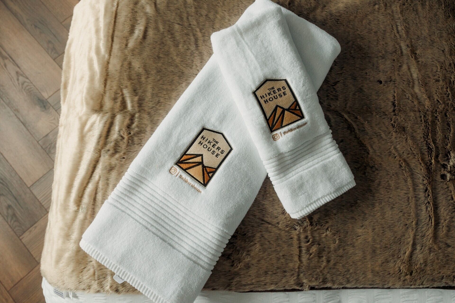 Twee witte handdoeken met geborduurde logo's op een houten ondergrond.