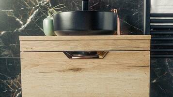 A wooden vanity with a black sink, a green vase, and a logo on the wall.