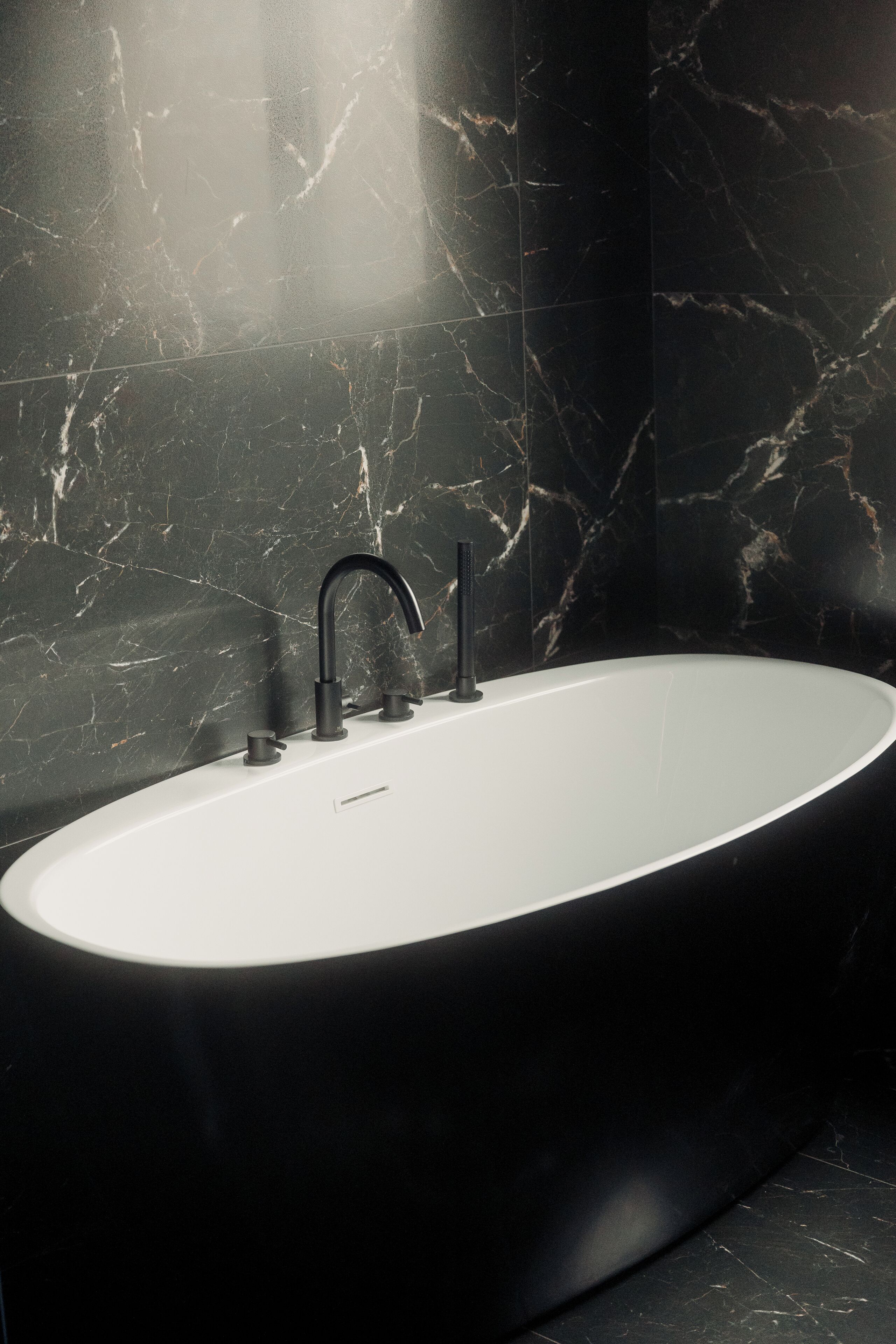 A modern bathroom with a freestanding bathtub, dark marble walls, and a sleek black faucet.