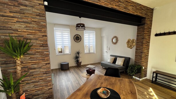 A modern living room with a wooden dining table, a grey sofa, and a black ceiling beam. - Quiet two-bedroom house on the banks of the Seine with parking space. Outdoor terrace (Cleon)