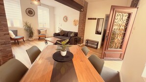 A modern living room with a wooden dining table, comfortable seating, a large plant, and a decorative mirror. - Quiet two-bedroom house on the banks of the Seine with parking space. Outdoor terrace (Cleon)
