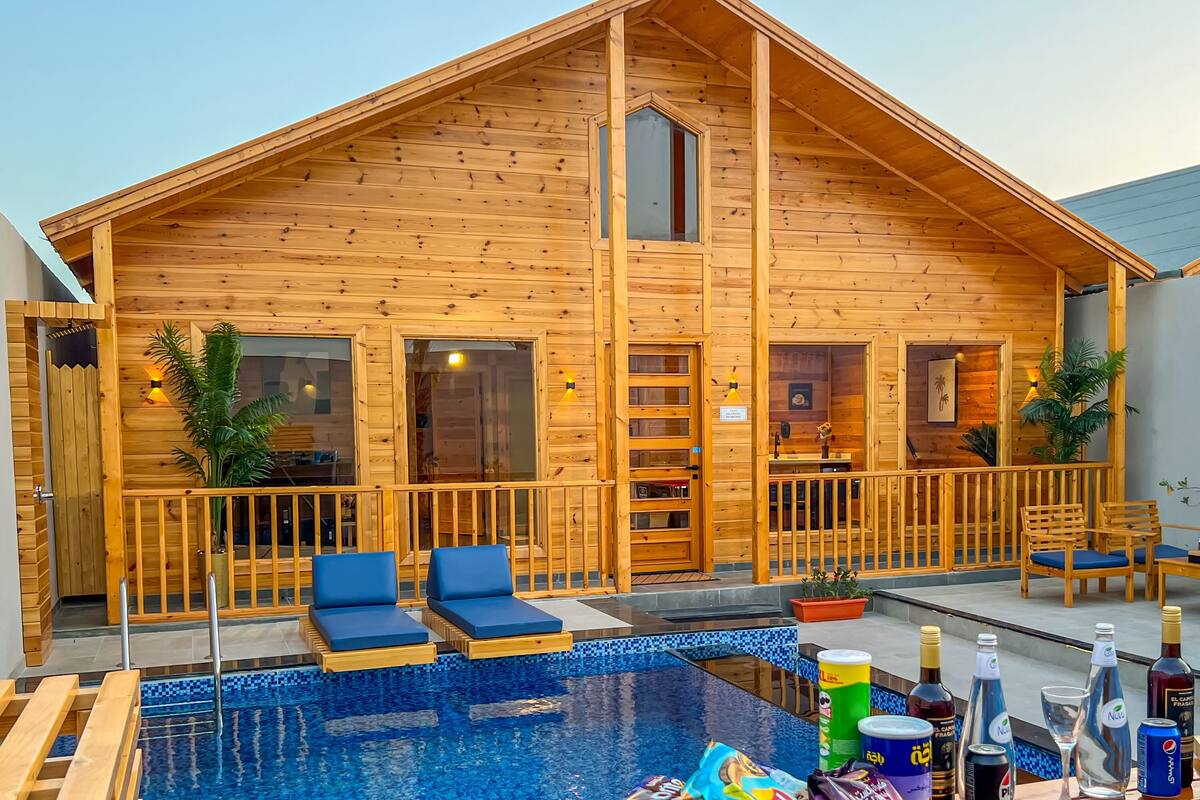 Una cabaña de madera con piscina, sillas de descanso y zona de comedor.