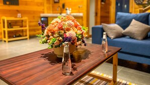 Een houten interieur met een bank, een houten salontafel met een bloemstuk, en een kleine tafel met een fles.