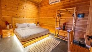 Een slaapkamer in een houten chalet, met een bed, nachtkastjes, een spiegel en een plank met toiletartikelen.