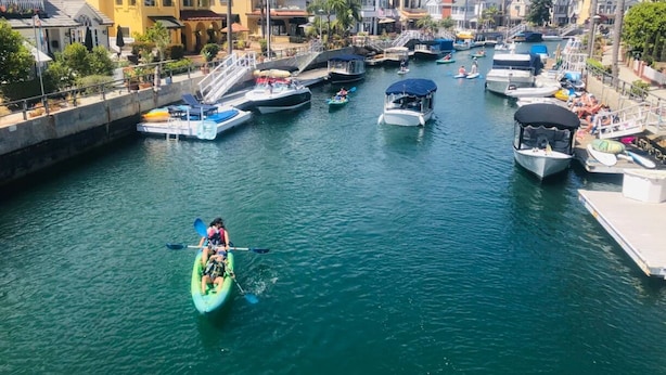 Un port de plaisance avec des bateaux amarrés, un kayak sur l’eau et des bâtiments en arrière-plan.