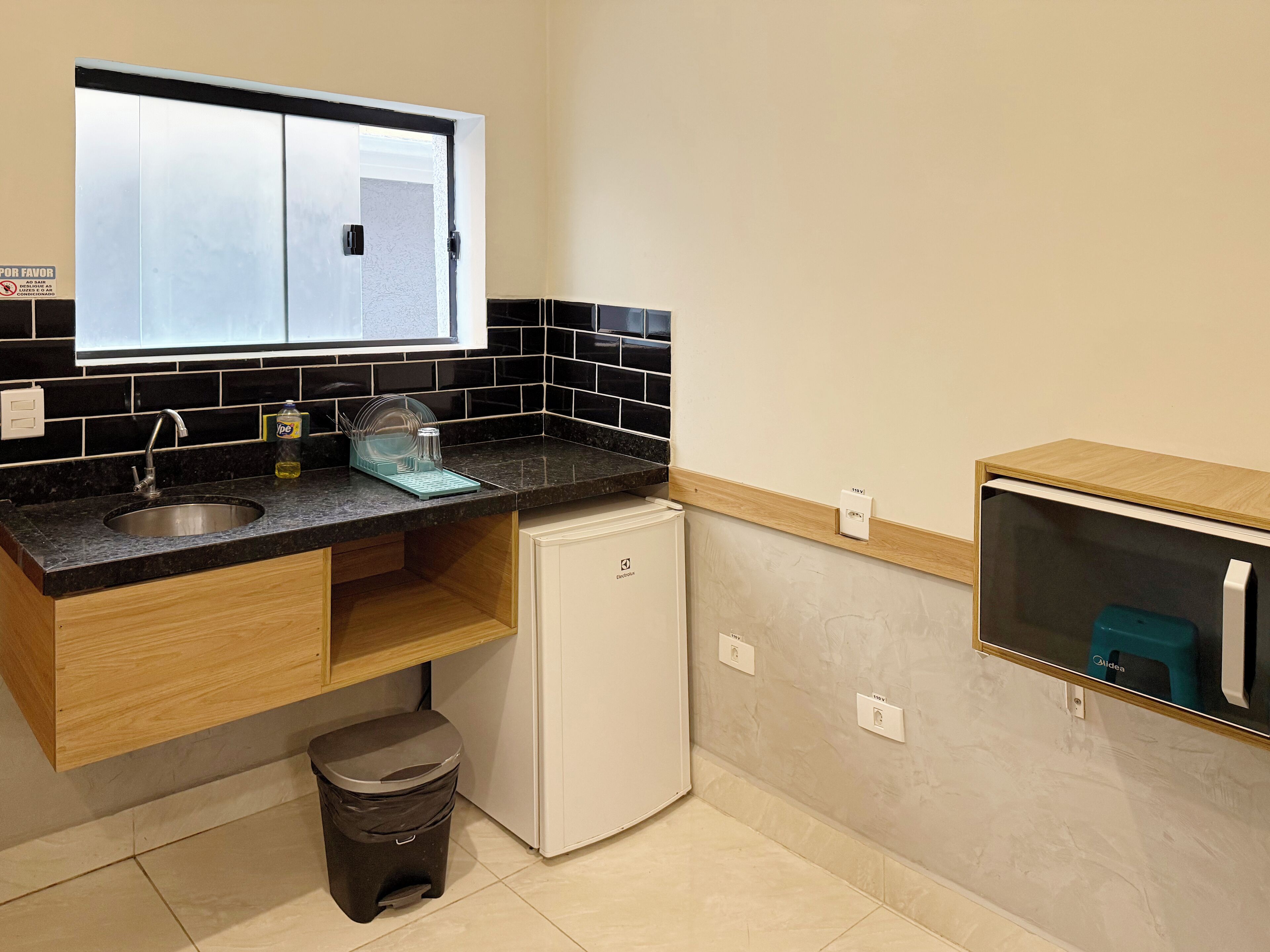 Cocina compacta con un lavamanos, un refrigerador pequeño y una ventana sobre la encimera.