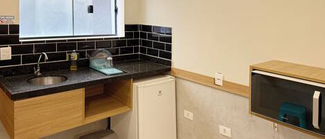 Cocina compacta con un lavamanos, un refrigerador pequeño y una ventana sobre la encimera.