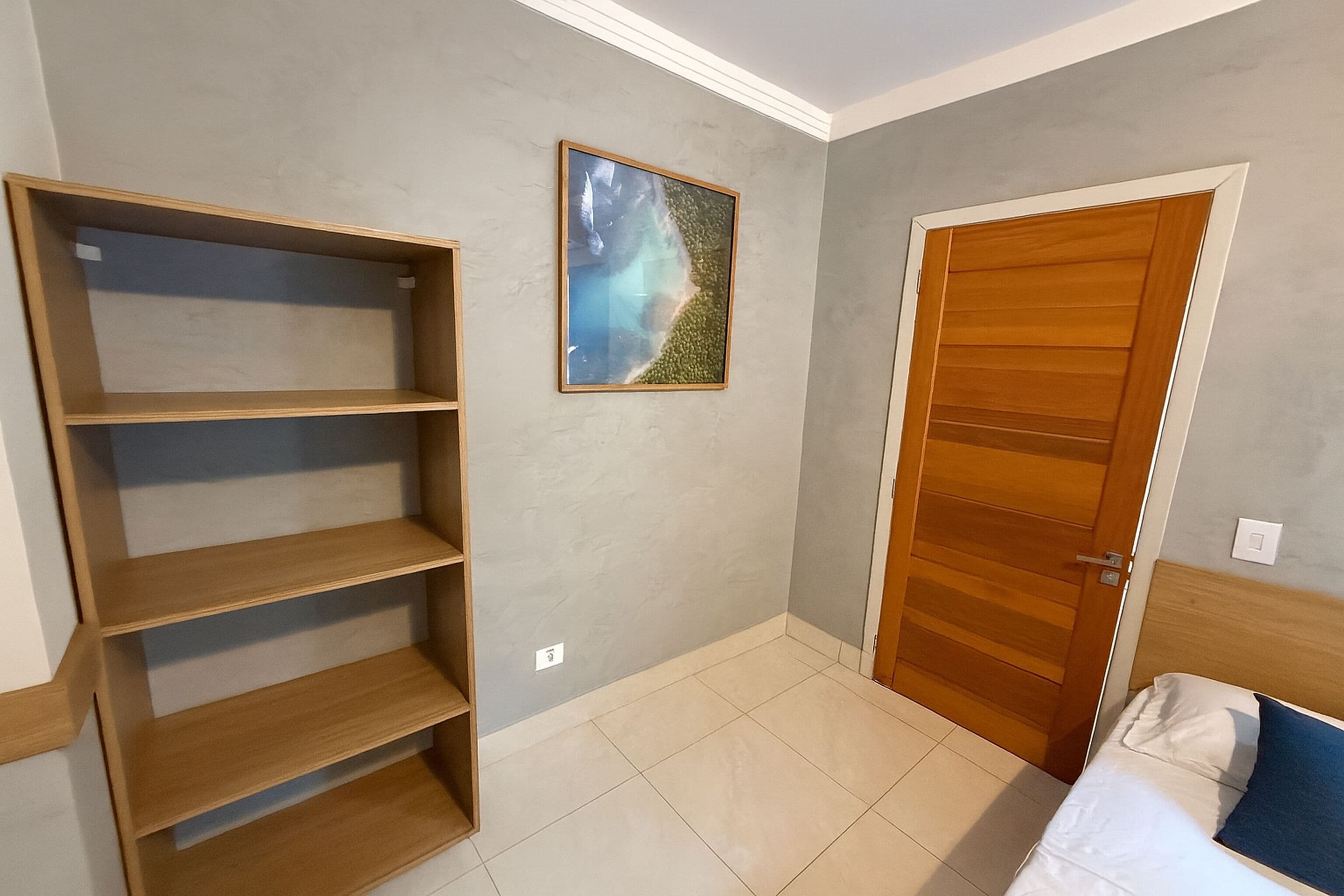 A room with a wooden wardrobe, a bed with white bedding, and a shelf unit.