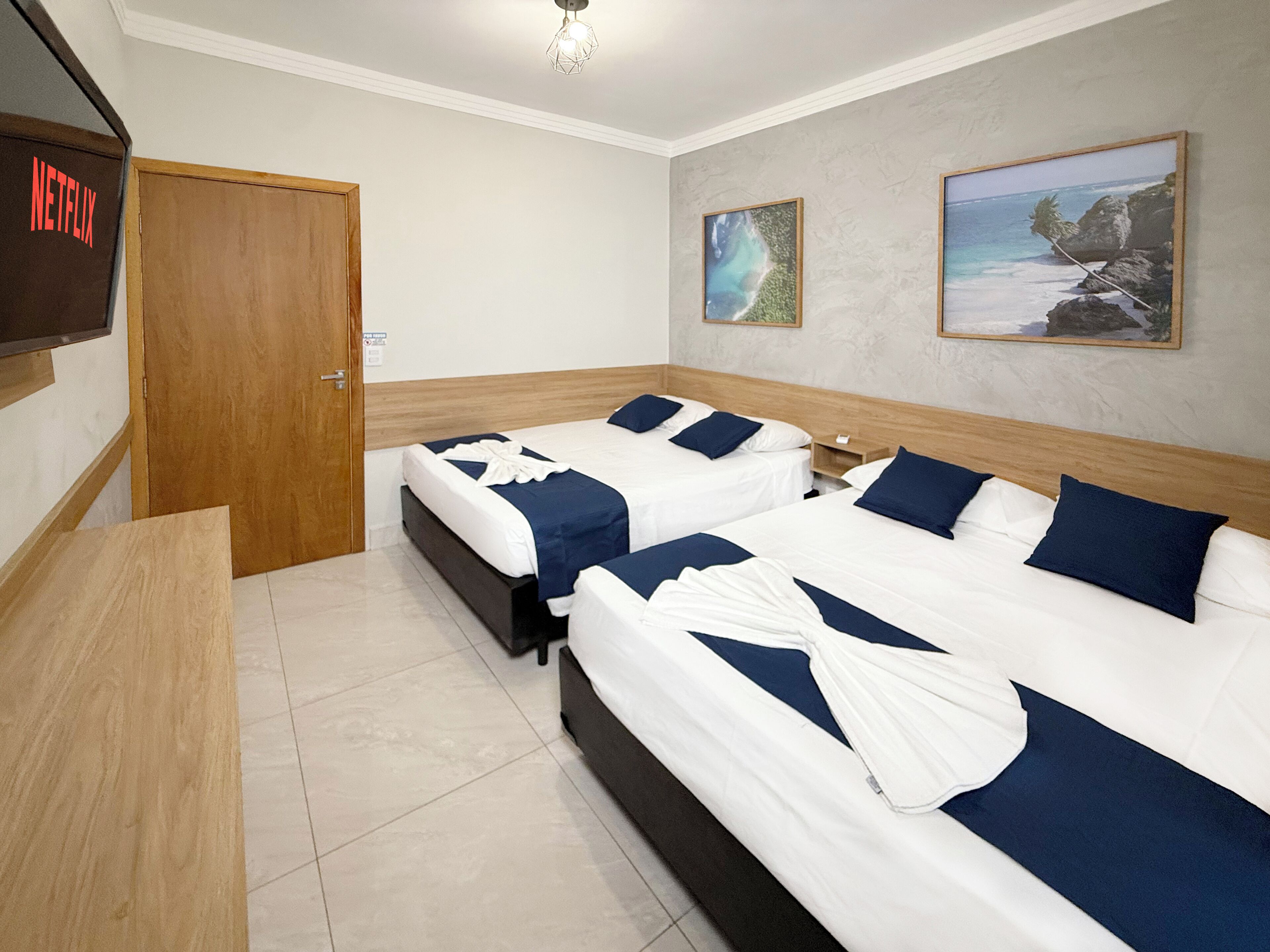 A hotel room with two beds, a TV, and two paintings on the wall.