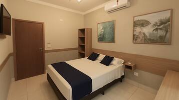 A bedroom with a bed, bedside table, nightstand, wall-mounted TV, and artwork.
