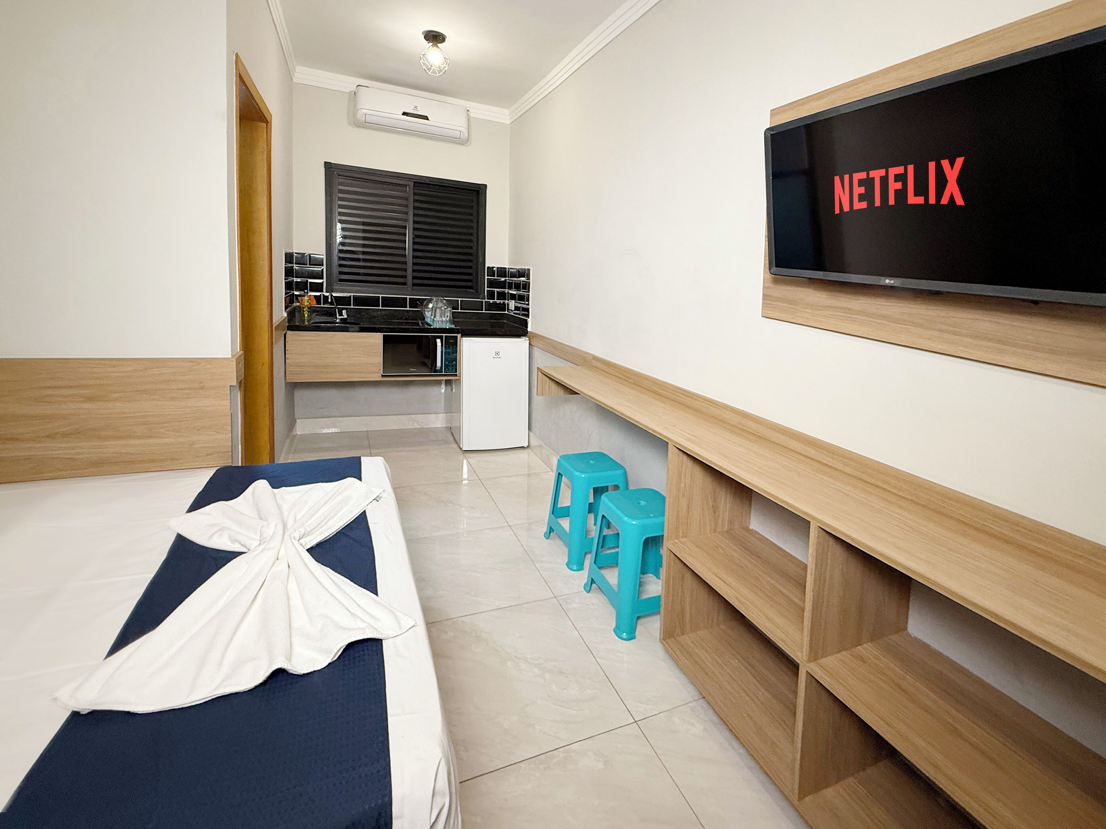 Una habitación de hotel con cama, televisor montado en la pared, kitchenette y escritorio con silla.