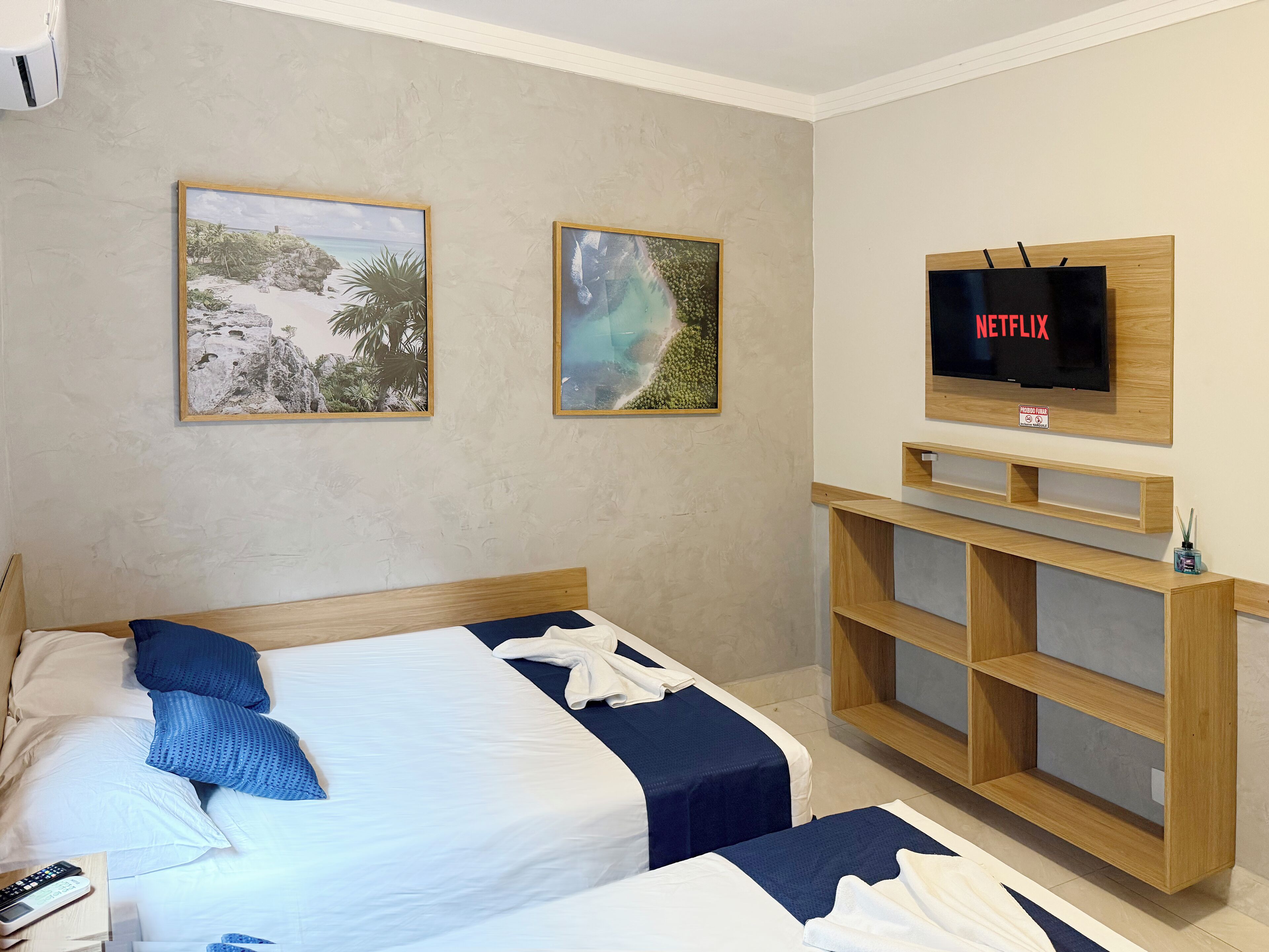 Ein Hotelzimmer mit zwei Betten, einem an einer Holzwand angebrachten Fernseher und zwei gerahmten Bildern.