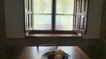 Una habitación con una mesa de madera, una ventana con contraventanas abiertas y vistas a la vegetación.