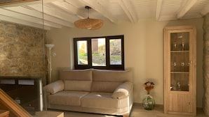 Ein Wohnzimmer mit einem beigen Sofa, einer Holzkabine mit Glastüren, einer Steinwand und einem Fenster mit Blick auf einen Garten.