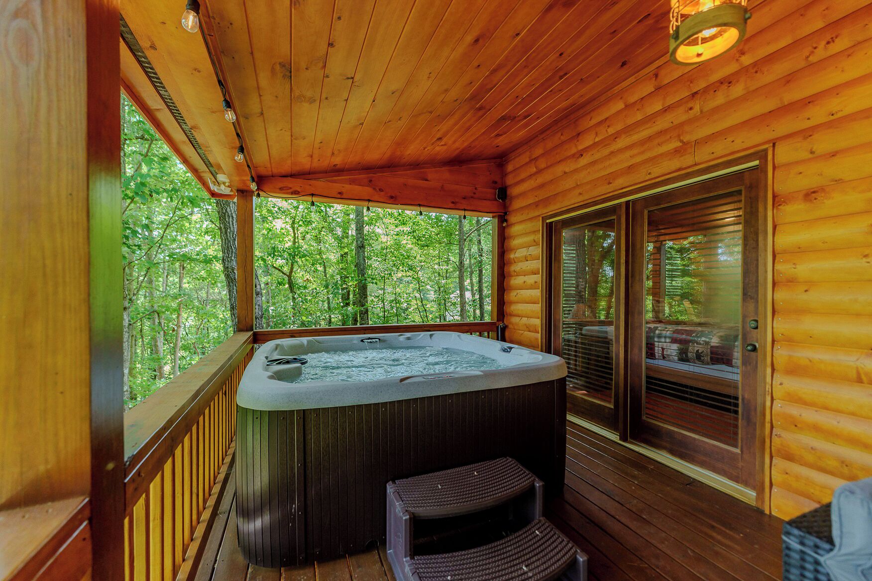 Une cabane en bois dotée d’un bain à remous, d’une terrasse et d’une porte vitrée donnant sur une zone boisée.