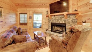 A log cabin interior with a stone fireplace, wooden walls, and a television mounted above it.
