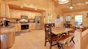 A spacious wooden cabin with a kitchen featuring stainless steel appliances, a dining area with wooden tables and chairs, and a ceiling fan.