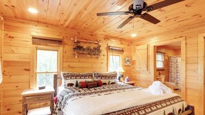 A wooden cabin bedroom with a bed, a nightstand, a desk, and a ceiling fan. - Cottage w/ Hot Tub: 3 Mi to Downtown Blue Ridge! (Blue Ridge)