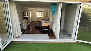 A room with a sliding glass door leading to a patio area. Inside, there is a foosball table, a sofa, and a television.