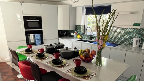 A modern kitchen with white cabinets, a central island with stools, a sink, and a window with a view of greenery.