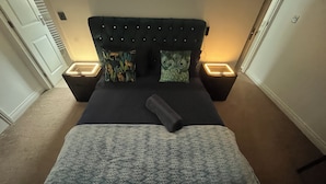 A neatly made bed with a patterned bedspread and a tufted headboard. There are two bedside tables with illuminated lamps.