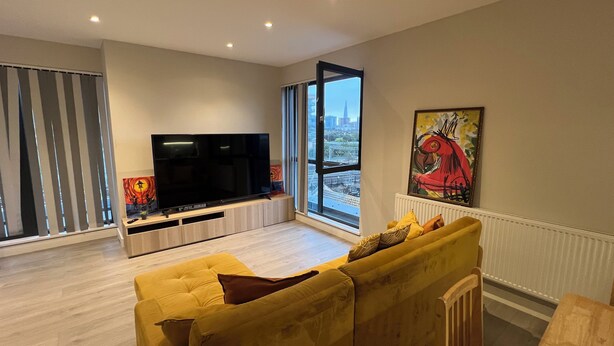 A modern living room with a large flat-screen TV, a yellow sofa, and a city view through large windows. - The Charm London  (Londres)