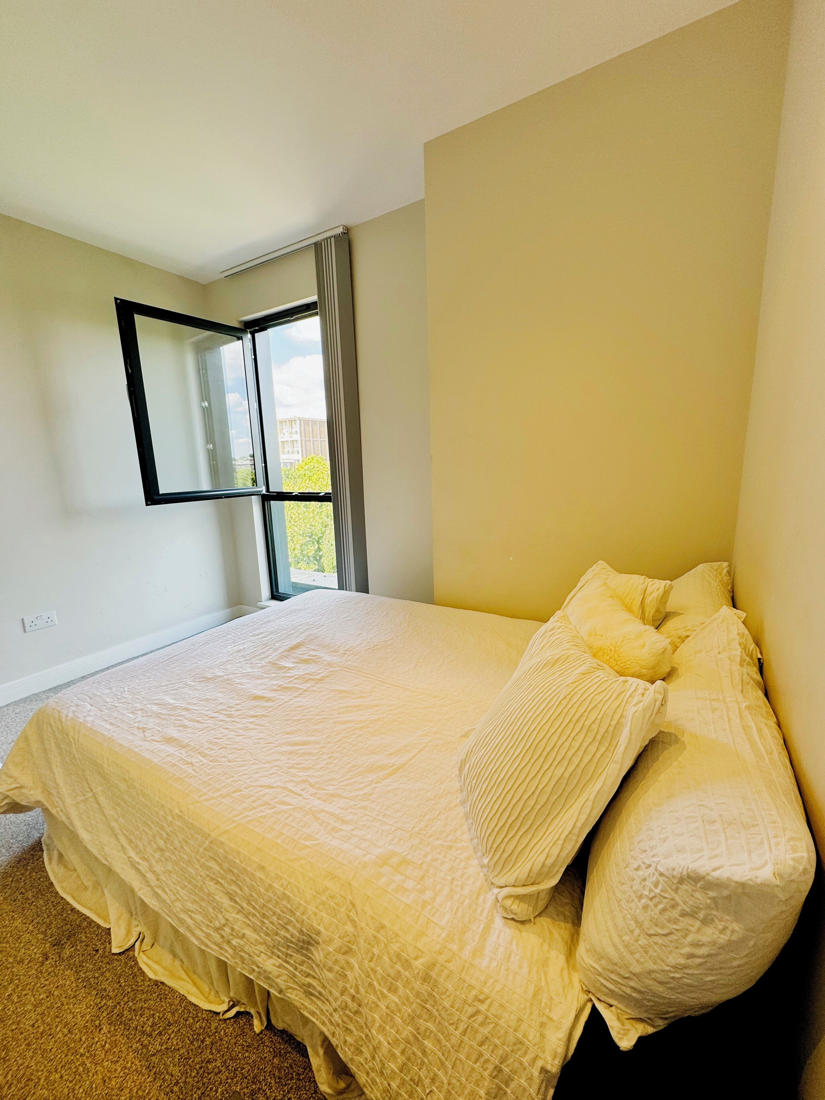 A bedroom with a bed, a window with curtains, and a wall-mounted mirror.