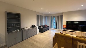A modern living room with a sofa, a TV, a coffee machine, and a bookshelf. - The Charm London  (Londres)