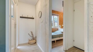 A hallway leading to a bedroom with a bed, a window, and a wooden floor. - Modern Chalet in the Veluwe (Putten)
