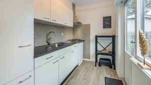 A modern kitchen with white cabinets, a granite countertop, and a black backsplash. There is a black shelf with decorative items and a small stool. - Modern Chalet in the Veluwe (Putten)