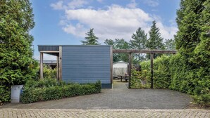 A covered outdoor area with a blue structure, paved walkway, and surrounding greenery. - Modern Chalet in the Veluwe (Putten)