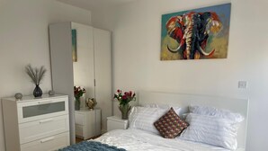 A bedroom with a bed, white wardrobe, bedside tables with flower vases, and a painting of an elephant.