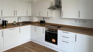 A modern kitchen with white cabinets, a stainless steel range hood, a built-in oven, and a wooden countertop.