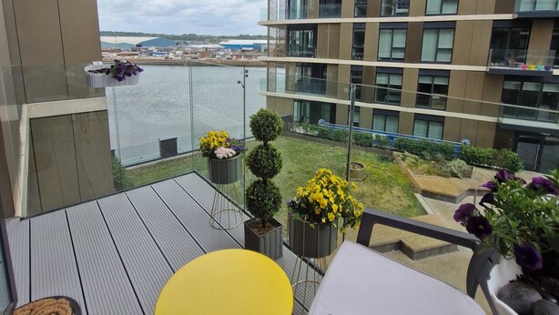 A balcony with a view of a river, a modern building, and a small garden area with potted plants.